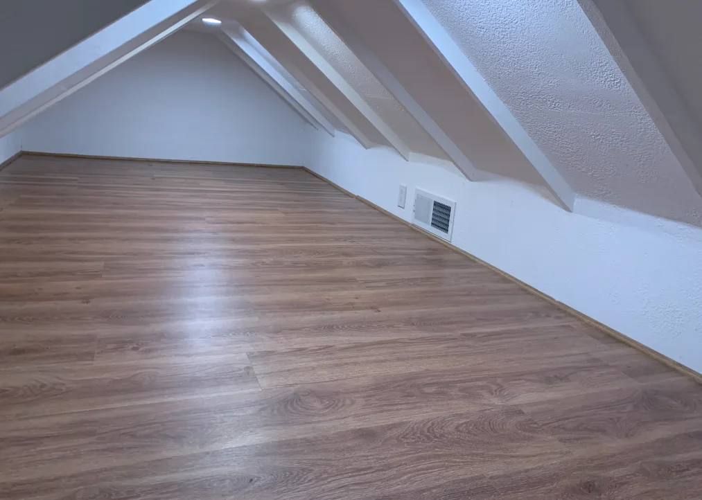 Finished low attic storage room with laminate flooring, white walls, and built-in vents.