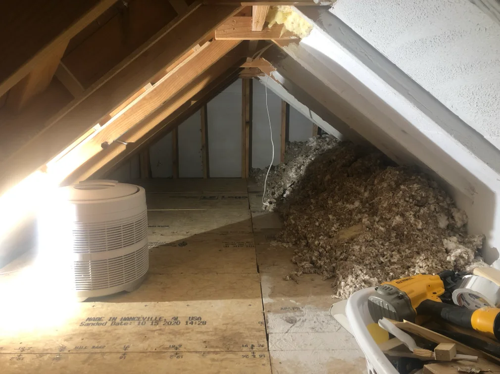 Unfinished low attic with exposed insulation, equipment, and a plywood walkway.