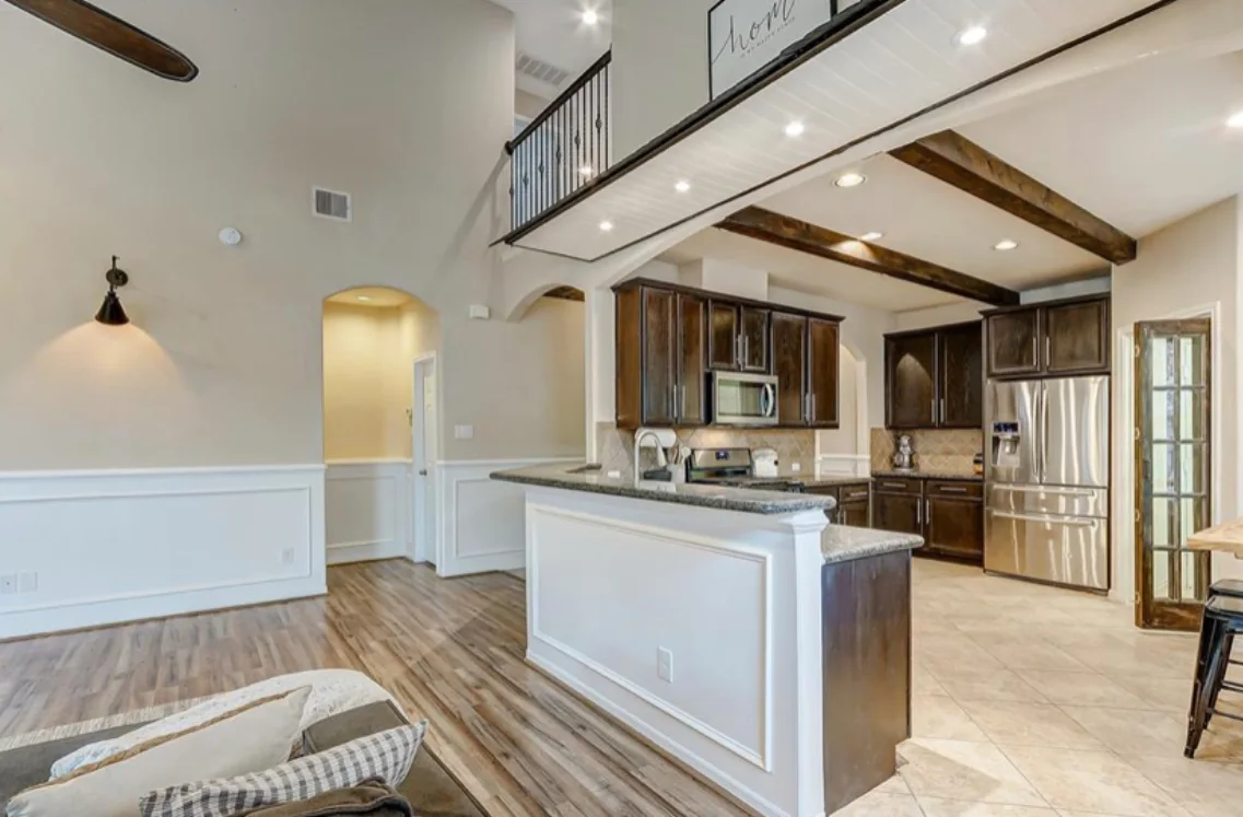 Open living room and kitchen with dark wood ceiling beams and recessed lighting.