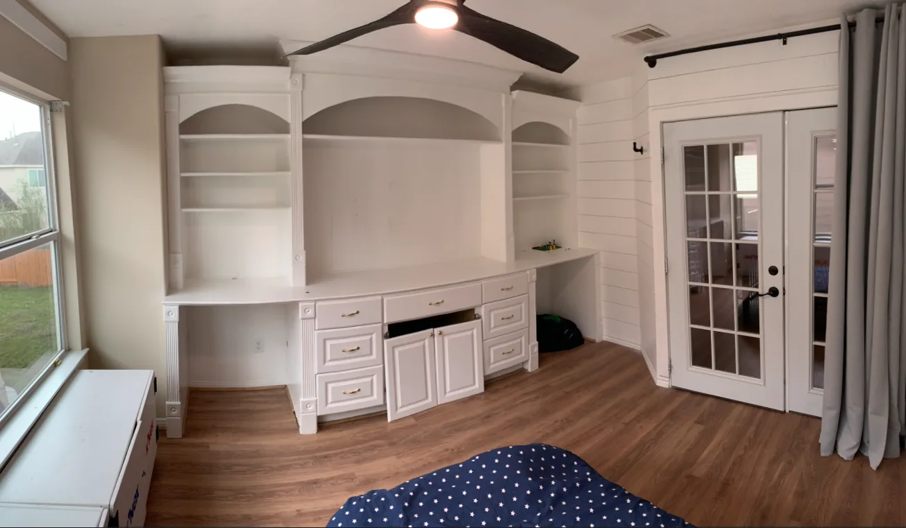 White built-in entertainment center, adjacent French door, shiplap wall, and laminate flooring.