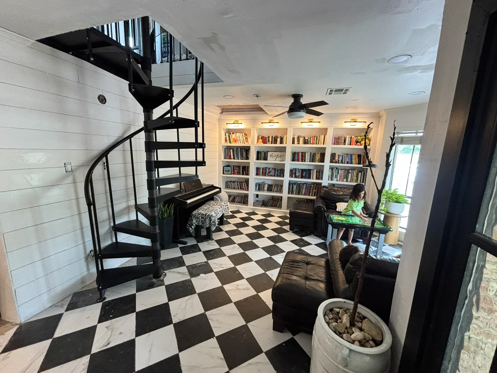 Black spiral staircase beside a lit built-in library and white shiplap walls.