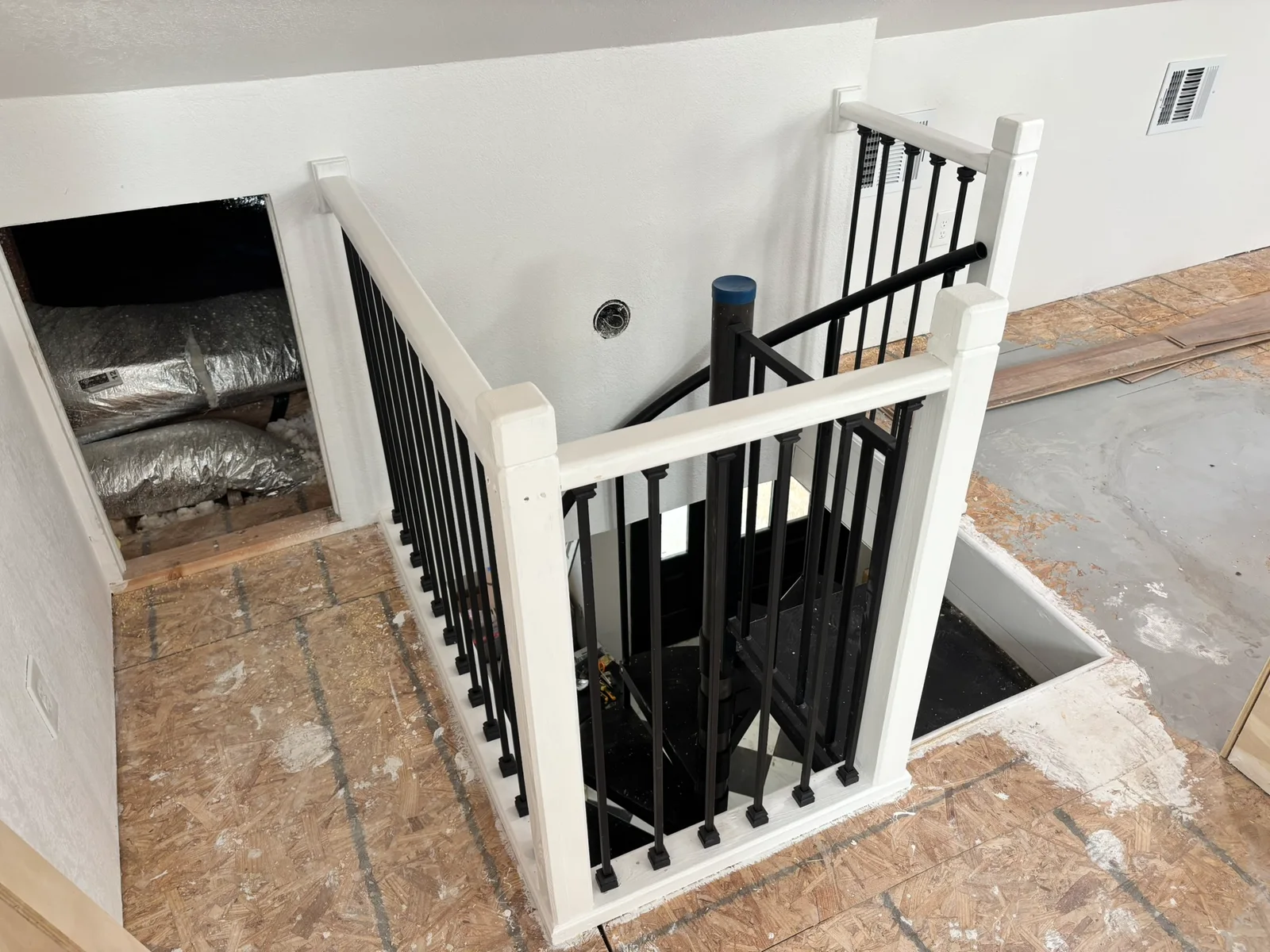 Upper landing view of the black spiral staircase with its white-and-black safety railing.